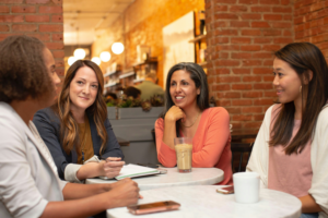 Four women sitting at table having a discussion.